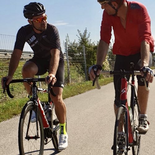 Auf diesem Bild sind zwei Radfahrer zu sehen, die an einem sonnigen Tag nebeneinander herfahren.