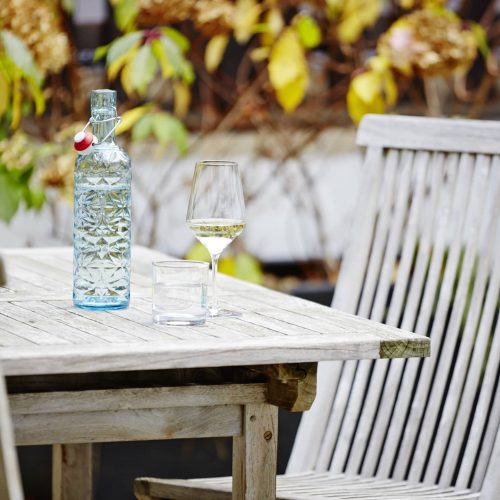 Auf diesem Bild sind Gartenmöbel, eine Flasche Wasser und ein Glas Wein zu sehen.