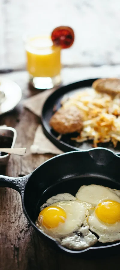 Herzhaftes Frühstück mit Eiern in der Pfanne, Toast, Röstbrot, Wurst, Marmelade und Orangensaft.