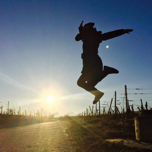 Auf diesem Bild ist zu sehen, dass eine Person vor Freude in die Luft springt. Dahinter ist der Sonnenuntergang zu sehen.